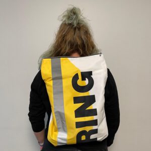 Eine Person trägt einen Rucksack, der aus den Farben gelb, weiß und grau besteht. 